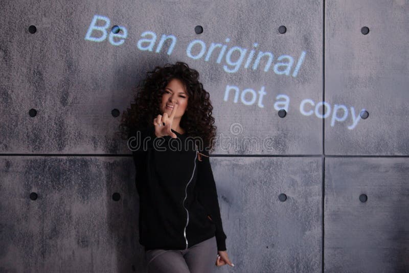 Mujer rizada posando activamente sobre un fondo de pared de concreto. La inscripciÃ³n coloreada se proyecta en la pared fotografía de archivo