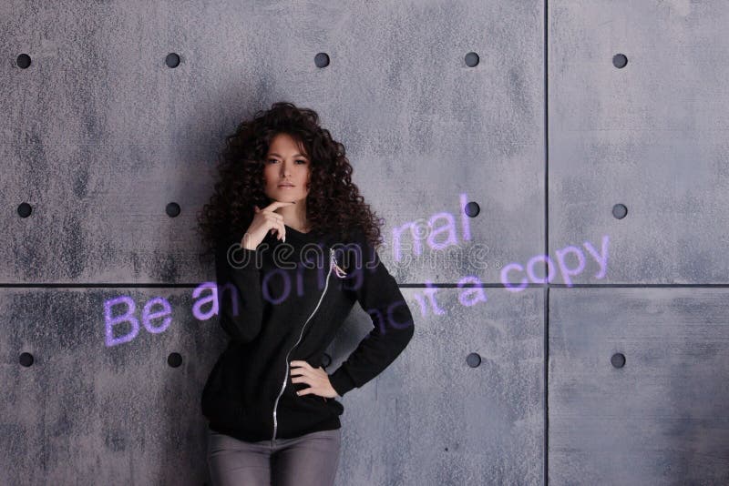 Mujer rizada posando activamente sobre un fondo de pared de concreto. La inscripciÃ³n coloreada se proyecta en la pared imagen de archivo