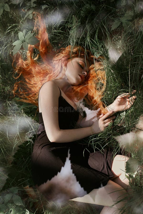 Mujer romántica con el pelo rojo que miente en la hierba en el bosque Una muchacha en sueños negros ligeros y sueños de un vestid fotografía de archivo Mujer romántica con el pelo rojo que miente en la hierba en el bosque Una muchacha en sueños negros ligeros y sueños de un vestid fotografía de archivo