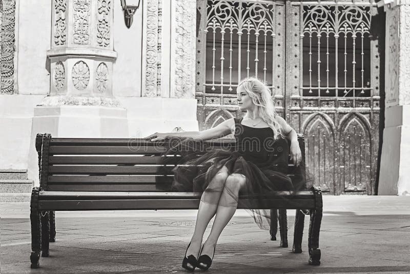 Mujer rubia elegante joven hermosa en el vestido negro que se sienta en a fotografía de archivo Mujer rubia elegante joven hermosa en el vestido negro que se sienta en a fotografía de archivo