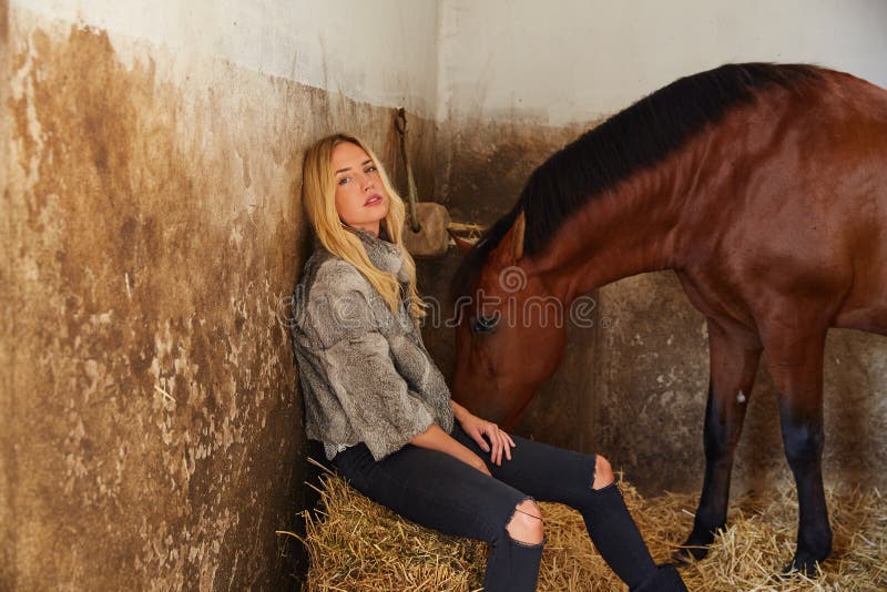 Mujer rubia en un establo interior con el caballo fotografía de archivo libre de regalías Mujer rubia en un establo interior con el caballo fotografía de archivo libre de regalías