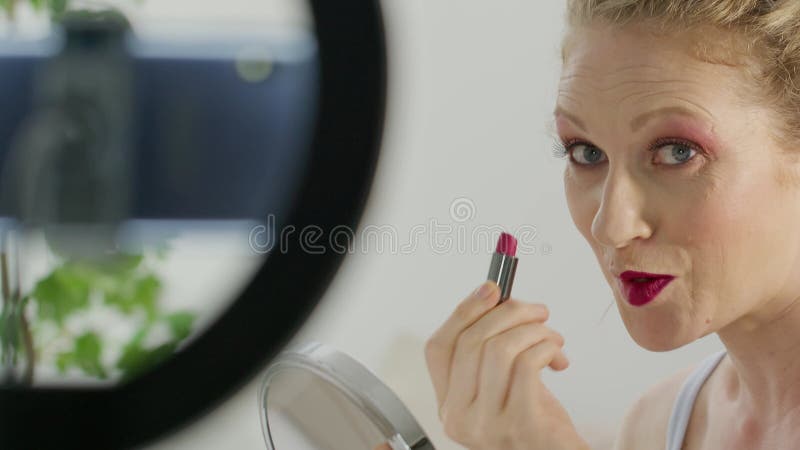 Mujer rubia sonriente influenciante blogger grabando un video tutorial en la cámara de un smartphone que muestra cómo aplicar cosm metrajes
