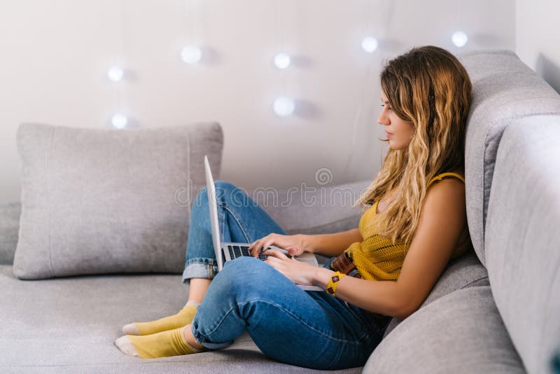 Mujer rubia trabajando en casa con una laptop sentada en el sofá en casa. fotos de archivo libres de regalías