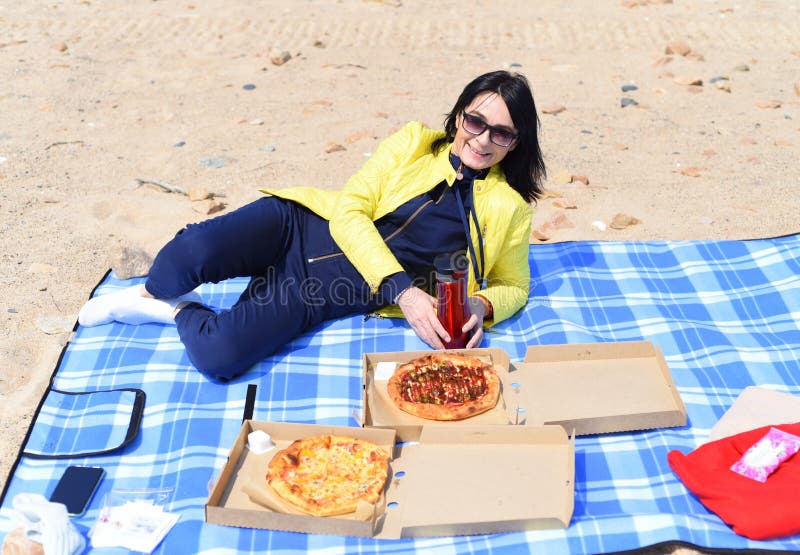 Mujer rusa de 45 años que va a comer pizza mientras está sentada en la playa fotografía de archivo libre de regalías