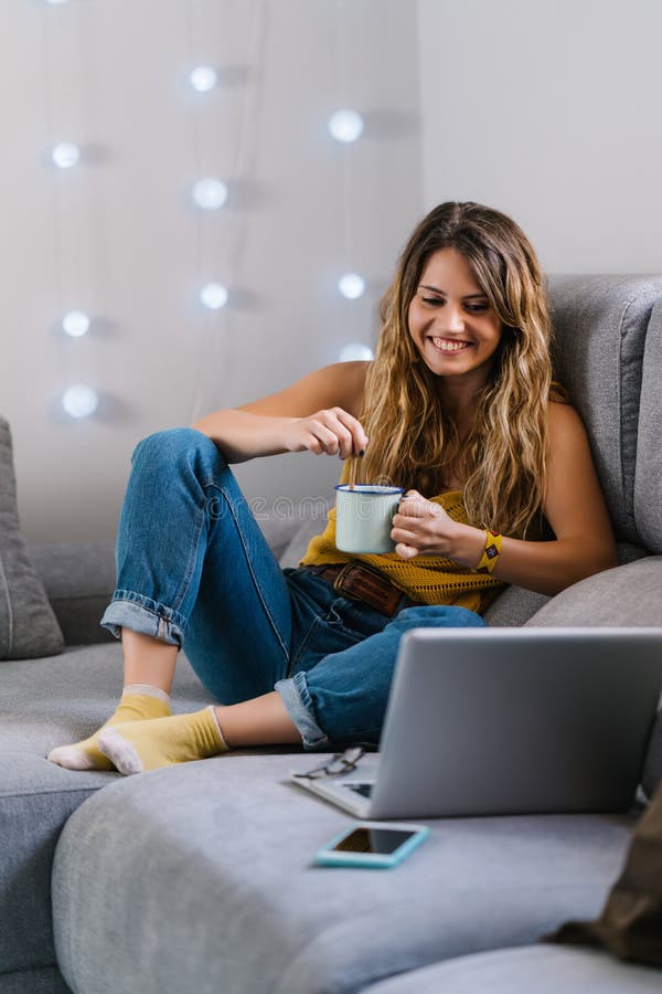 Mujer sentada en un sofá usando un portátil y tomando café foto de archivo