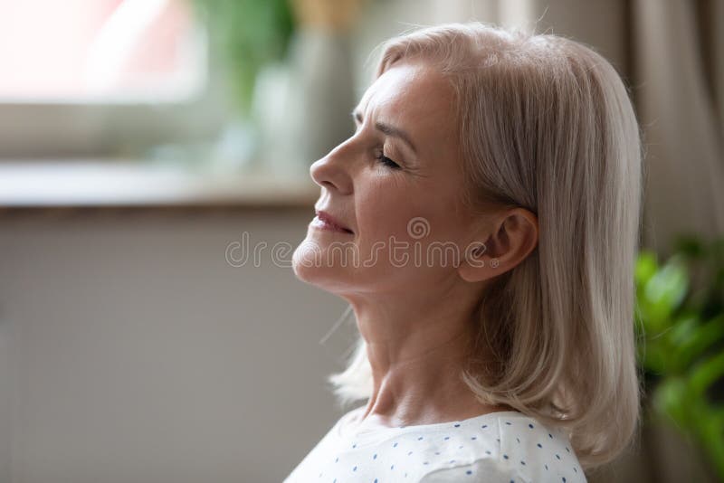 Mujer serena tranquila de mediana edad respirando con los ojos cerrados