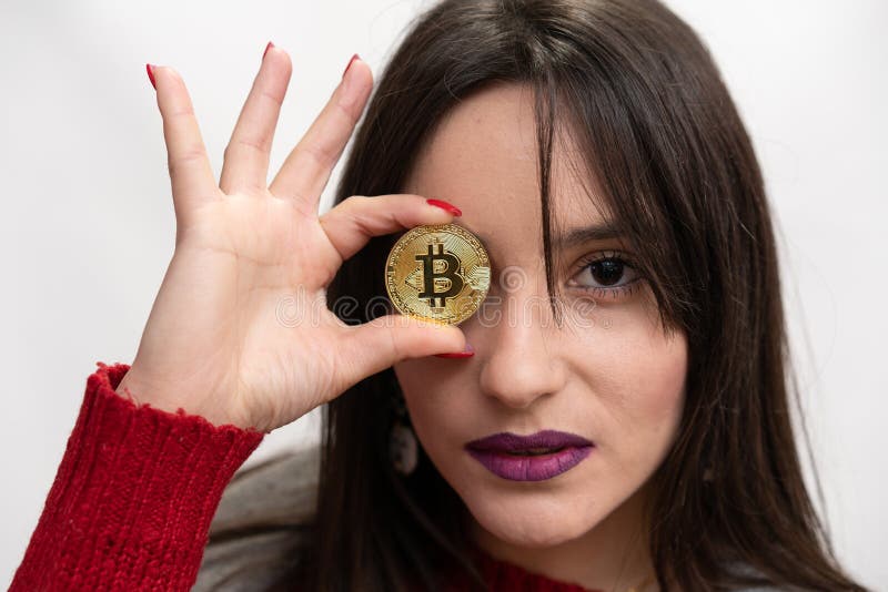 Mujer seria que sostiene un Bitcoin delante de su ojo derecho foto de archivo libre de regalías Mujer seria que sostiene un Bitcoin delante de su ojo derecho foto de archivo libre de regalías