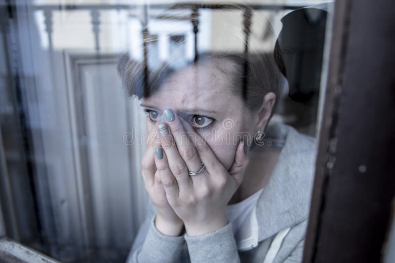 Mujer sola deprimida infeliz atractiva joven que mira la mirada triste a través de la ventana en casa imagenes de archivo Mujer sola deprimida infeliz atractiva joven que mira la mirada triste a través de la ventana en casa imagenes de archivo
