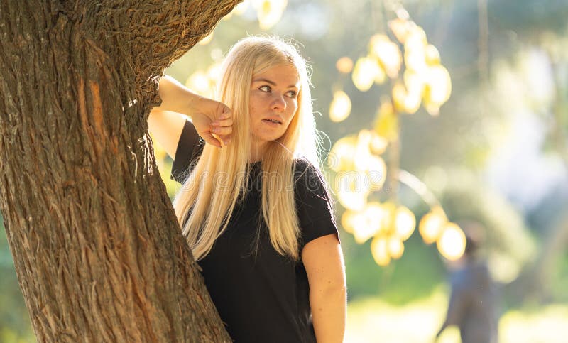 Mujer sonriente con cordones odontológicos apoyándose en un árbol en el parque foto de archivo libre de regalías