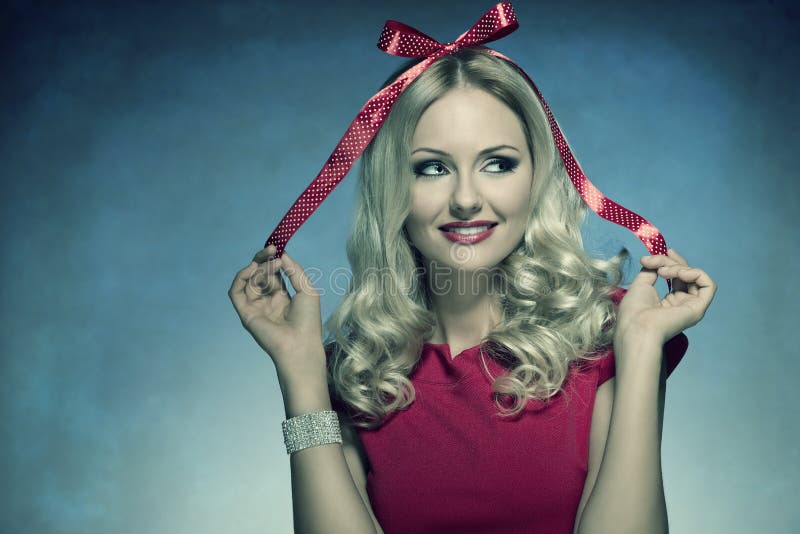 Mujer sonriente de Navidad con el arco. El retrato divertido del primer de la muchacha rubia linda con el arco de Navidad en su cabeza le gusta un regalo, de un vestido elegante rojo que lleva y de una pulsera brillante