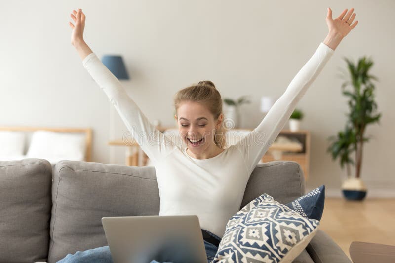 Mujer sonriente emocionada que celebra triunfo en línea, usando el ordenador portátil en casa
