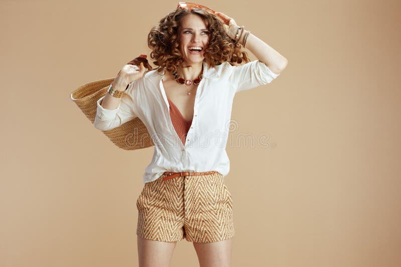 Mujer sonriente en blusa y pantalones cortos saltando sobre beige