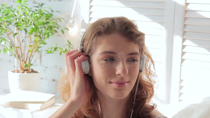 Mujer sonriente joven que escucha la música con los auriculares en una mañana soleada