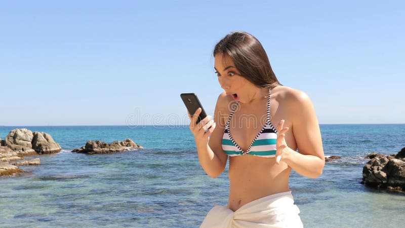 Mujer sorprendida en contenido del teléfono de la lectura del bikini en la playa