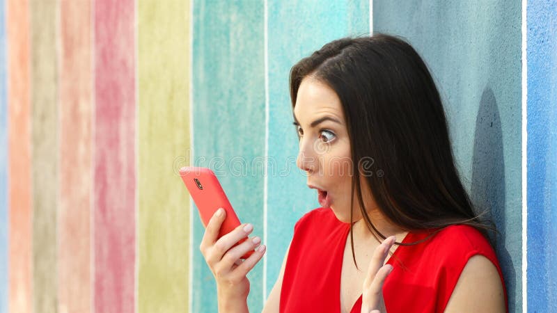 Mujer sorprendida que comprueba el teléfono en una pared colorida