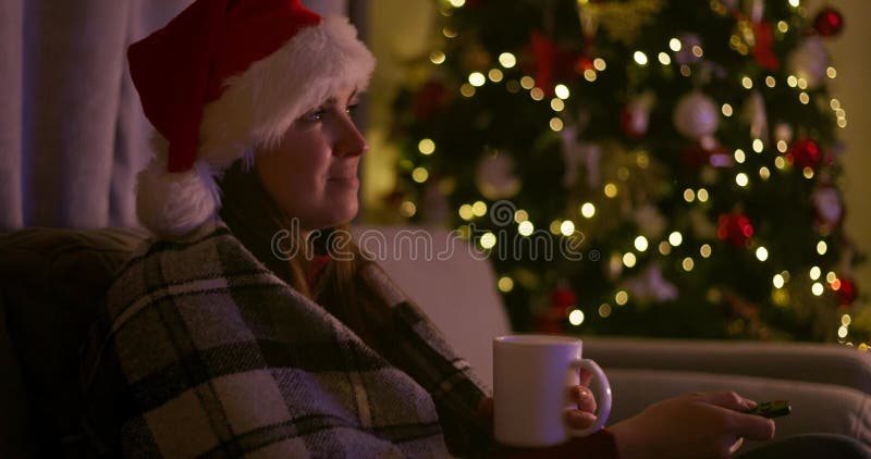 Mujer sosteniendo una taza sentada en un sofá con una manta mirando televisión metrajes