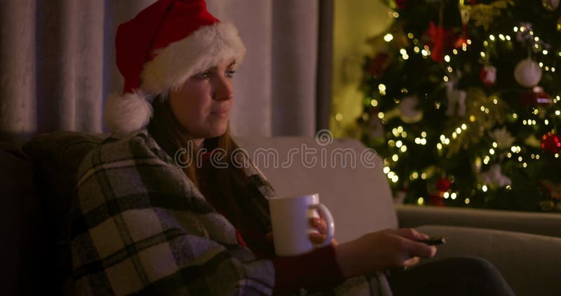Mujer sosteniendo una taza sentada en un sofá con una manta mirando televisión metrajes