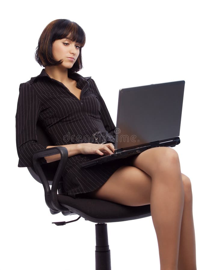 Concentrated brunette woman in dark dress sitting in the office chair and working on laptop over white background. Concentrated brunette woman in dark dress sitting in the office chair and working on laptop over white background