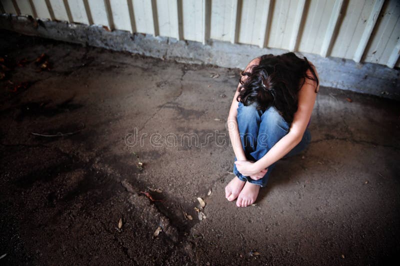 A sad woman is sitting alone on the cold concrete behind a shed. A sad woman is sitting alone on the cold concrete behind a shed