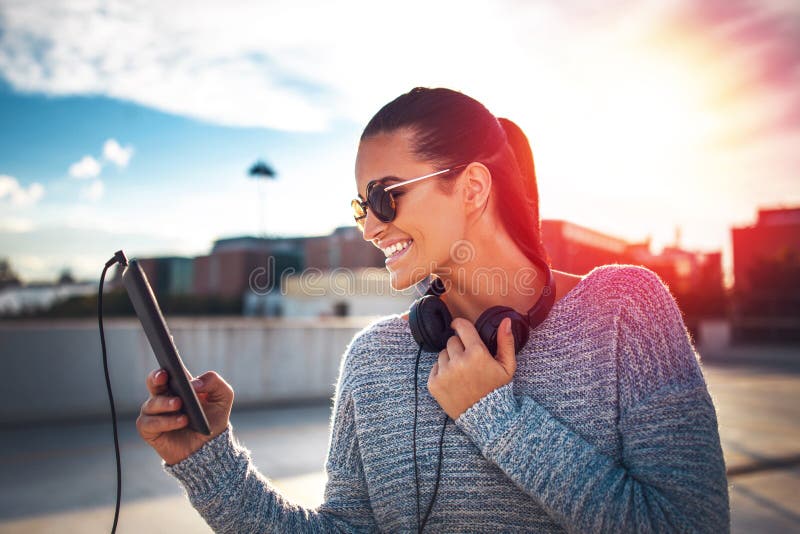Mujer urbana joven de moda feliz con la tableta en puesta del sol fotografía de archivo Mujer urbana joven de moda feliz con la tableta en puesta del sol fotografía de archivo