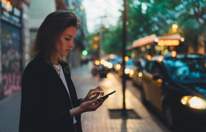 Traveler woman calling mobile phone waiting yellow taxi in evening street europe city Barcelona. Girl tourist using smartphone internet online gadget cellphone on background bokeh headlights of cars. Traveler woman calling mobile phone waiting yellow taxi in evening street europe city Barcelona. Girl tourist using smartphone internet online gadget cellphone on background bokeh headlights of cars