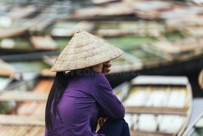 Mujer vietnamita que lleva la localización cónica del sombrero de la camiseta larga púrpura del brazo y que espera en la tierra t fotos de archivo libres de regalías Mujer vietnamita que lleva la localización cónica del sombrero de la camiseta larga púrpura del brazo y que espera en la tierra t fotos de archivo libres de regalías