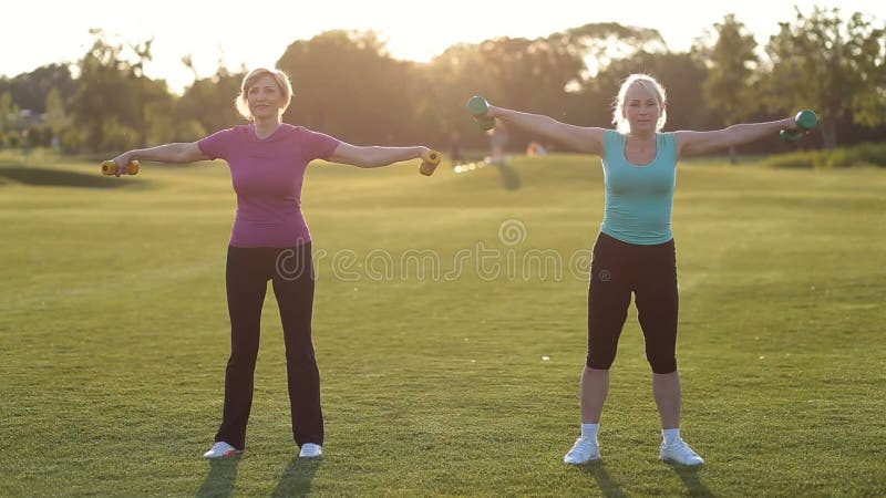 Mujeres adultas deportivas con las pesas de gimnasia que doblan los músculos