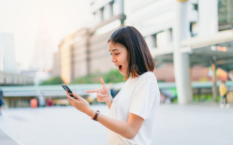 Mujeres asiáticas del teléfono elegante sonriente y que se considera feliz con sorprendido para el éxito imagen de archivo libre de regalías Mujeres asiáticas del teléfono elegante sonriente y que se considera feliz con sorprendido para el éxito imagen de archivo libre de regalías