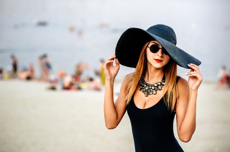 Hermosa mujer en ropa de verano negro apoyado contra una palmera en la  playa. mujer alegre con sombrero negro y ropa de verano negra posando.