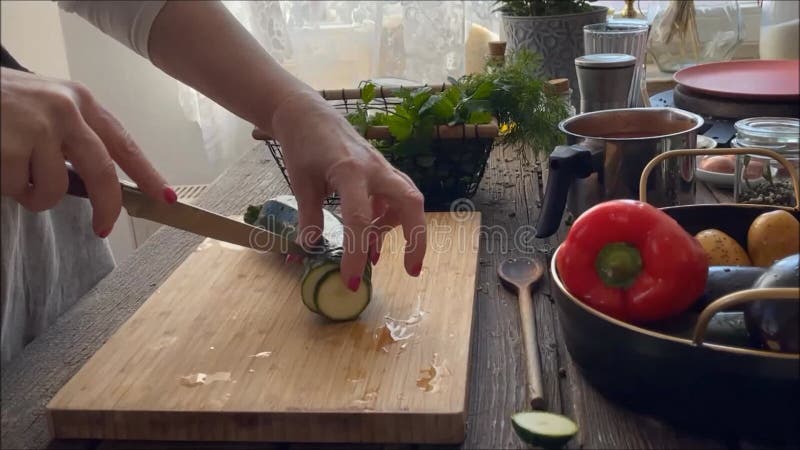Mujeres cortando zucchini en tablero de madera sobre mesa de cocina en la ventana