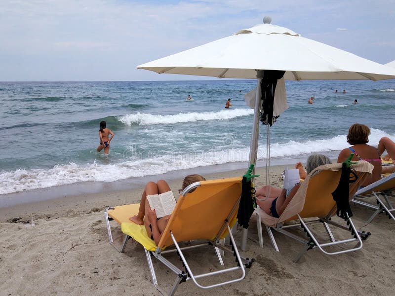 Mujeres debajo de los paraguas que se relajan en sunbeds mientras que otras personas que nadan imágenes de archivo libres de regalías Mujeres debajo de los paraguas que se relajan en sunbeds mientras que otras personas que nadan imágenes de archivo libres de regalías