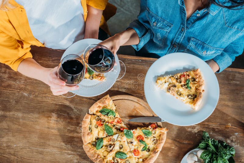 Mujeres jovenes que tintinean las copas de vino mientras que come la pizza hecha en casa junta