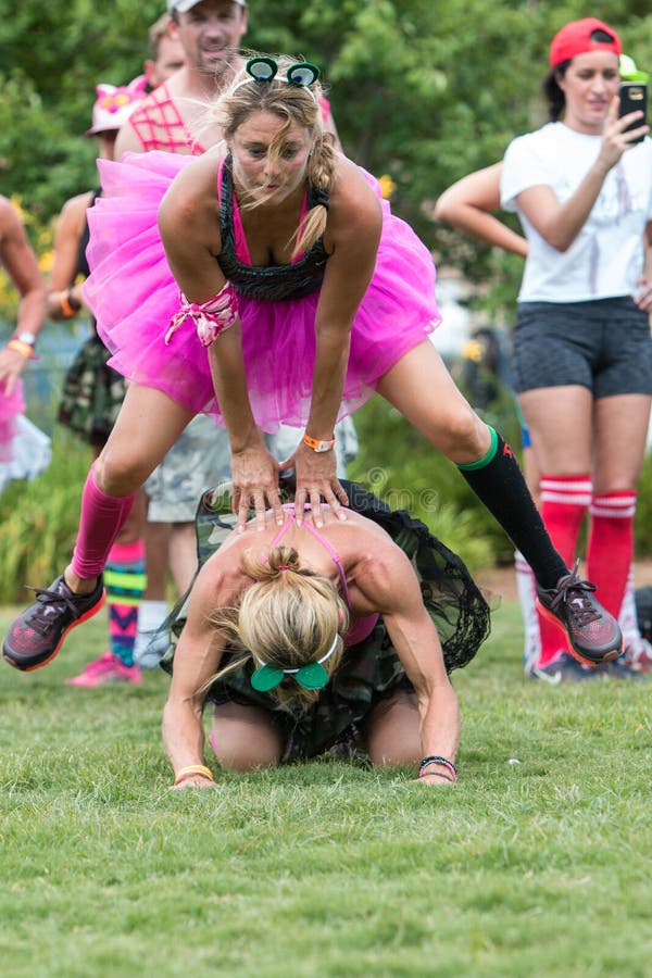 Mujeres que llevan la rana del salto del juego de los tutúes en el evento del día de maniobras fotografía de archivo Mujeres que llevan la rana del salto del juego de los tutúes en el evento del día de maniobras fotografía de archivo