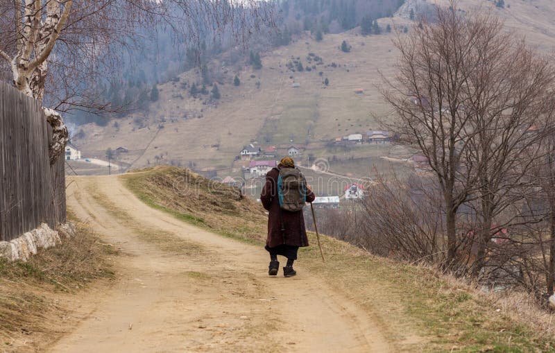 Mulher adulta que anda em uma estrada da aldeia da montanha imagem de stock Mulher adulta que anda em uma estrada da aldeia da montanha imagem de stock