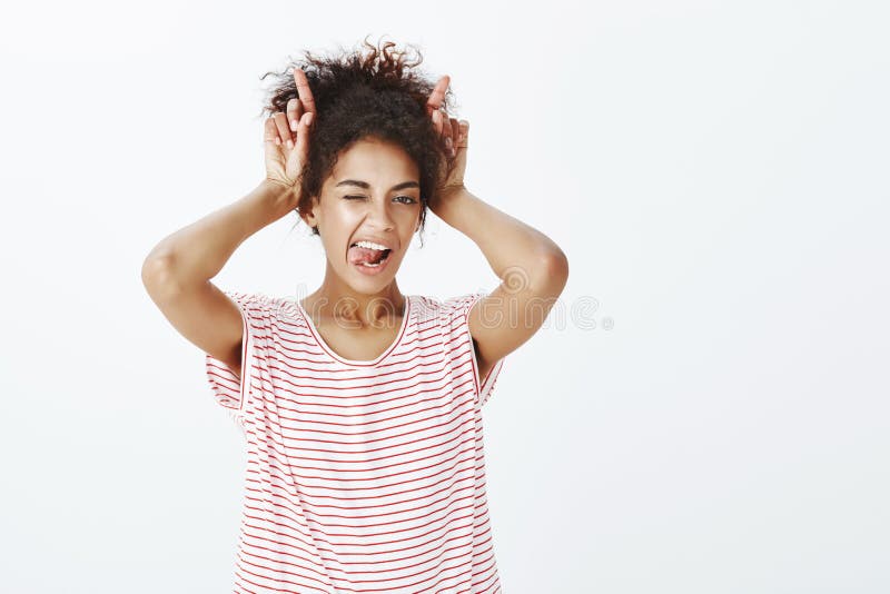 Mulher africana atrativa Sassy com penteado afro em t-shirt listrado, guardando o diabo de imitação aéreo dos indicadores fotos de stock Mulher africana atrativa Sassy com penteado afro em t-shirt listrado, guardando o diabo de imitação aéreo dos indicadores fotos de stock