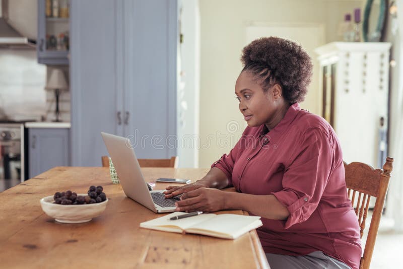 Mulher africana nova que senta em casa o trabalho em um portátil fotografia de stock royalty free Mulher africana nova que senta em casa o trabalho em um portátil fotografia de stock royalty free