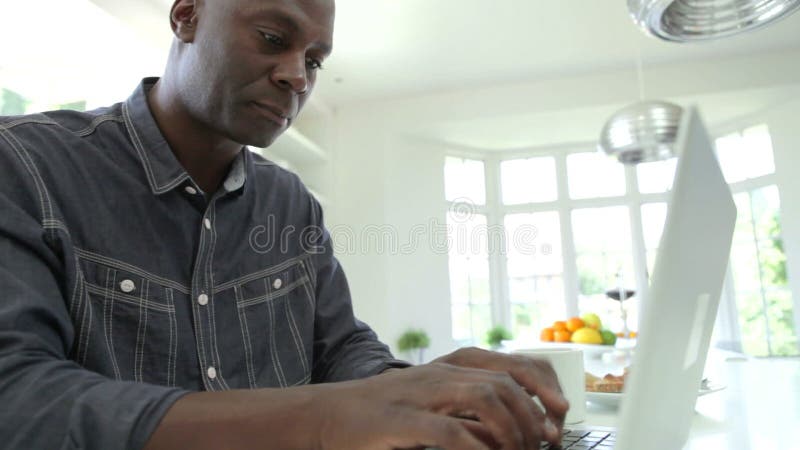 Mulher afro-americano que usa o portátil na cozinha em casa