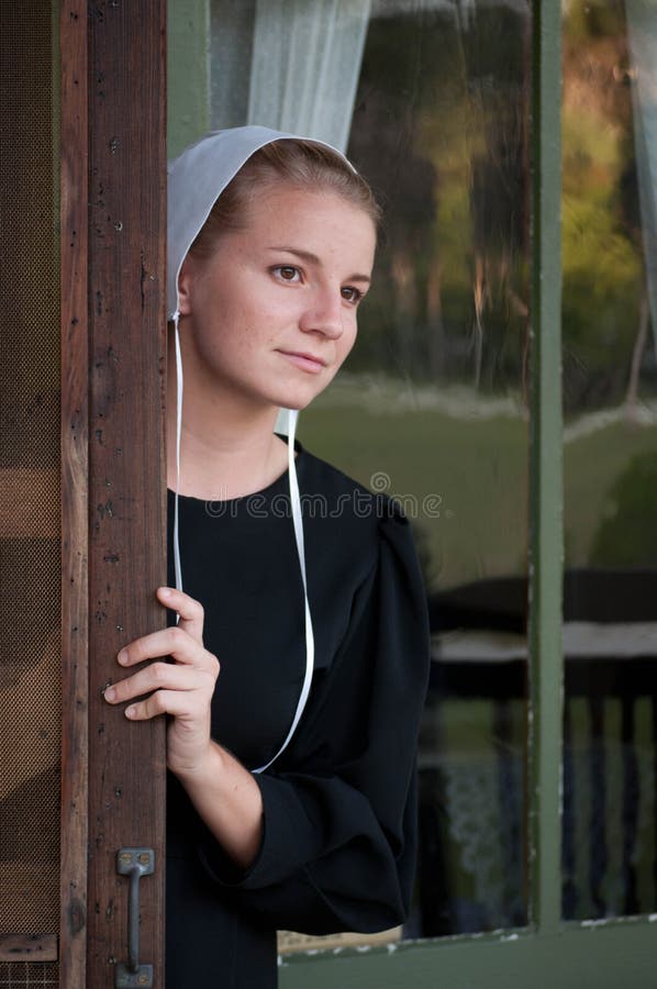 A mulher Amish olha para fora a porta de tela
