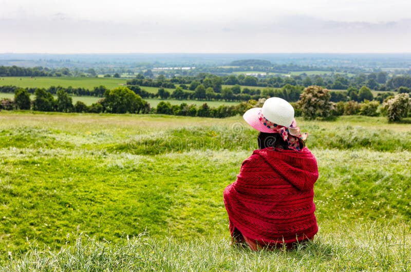 A mulher aprecia a vista de terras de exploração agrícola ao sentar-se para baixo no campo imagem de stock royalty free A mulher aprecia a vista de terras de exploração agrícola ao sentar-se para baixo no campo imagem de stock royalty free