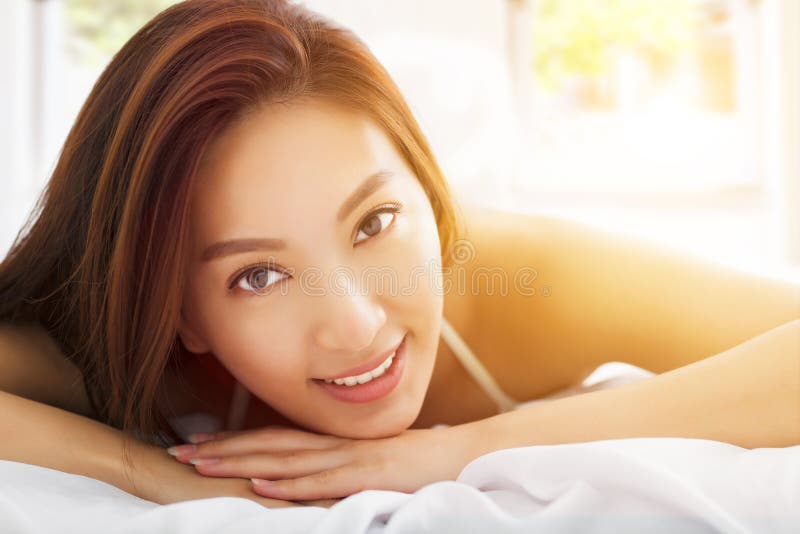 Mulher asiática bonita que relaxa na cama com vagabundos da luz solar fotos de stock royalty free Mulher asiática bonita que relaxa na cama com vagabundos da luz solar fotos de stock royalty free