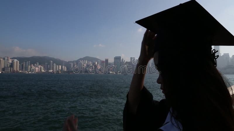 Mulher asiática colocou a tampa da graduação no horizonte hong kong kong na frente da água