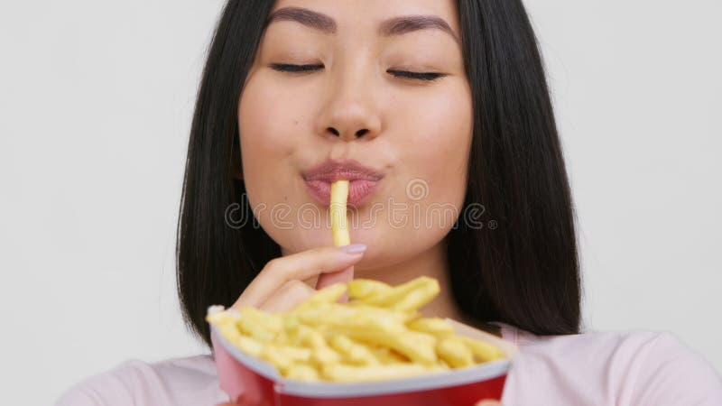 Mulher asiática comendo batatas fritas fritas desfrutando de comida-lixo como fundo branco