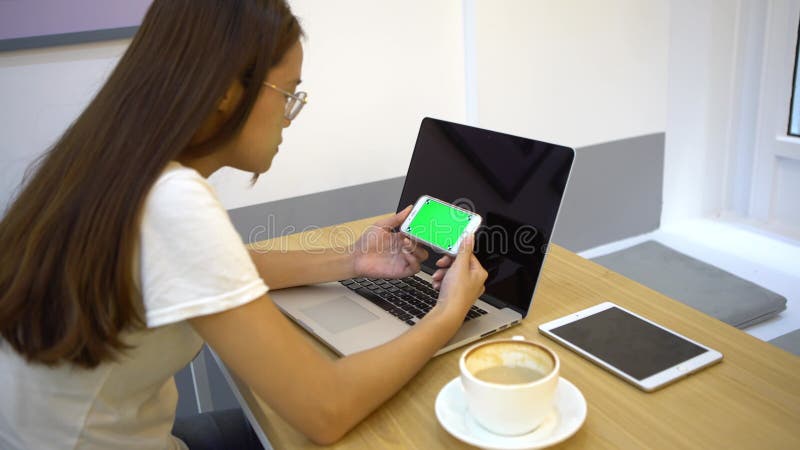 Mulher asiática de 4k usando um smartphone e laptop de tela verde em um café