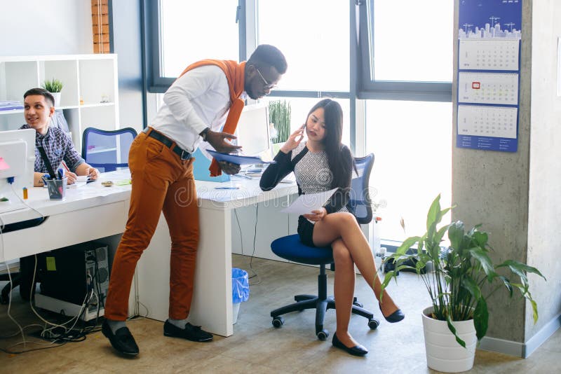 A mulher asiática está mostrando o original ao assistente africano ao falar no smartphone fotos de stock A mulher asiática está mostrando o original ao assistente africano ao falar no smartphone fotos de stock