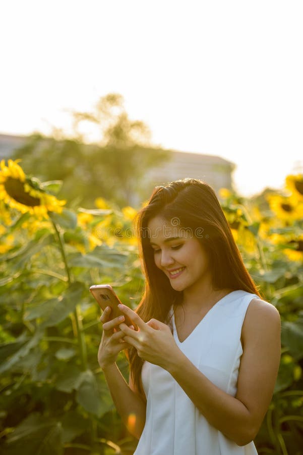 Mulher asiática feliz nova que sorri ao usar o telefone celular no imagens de stock Mulher asiática feliz nova que sorri ao usar o telefone celular no imagens de stock