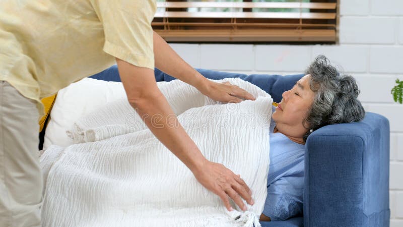 Mulher asiática idosa dormindo no sofá e seu marido cobrindo cobertor, homem asiático conforto e cuidado enquanto mulher idosa