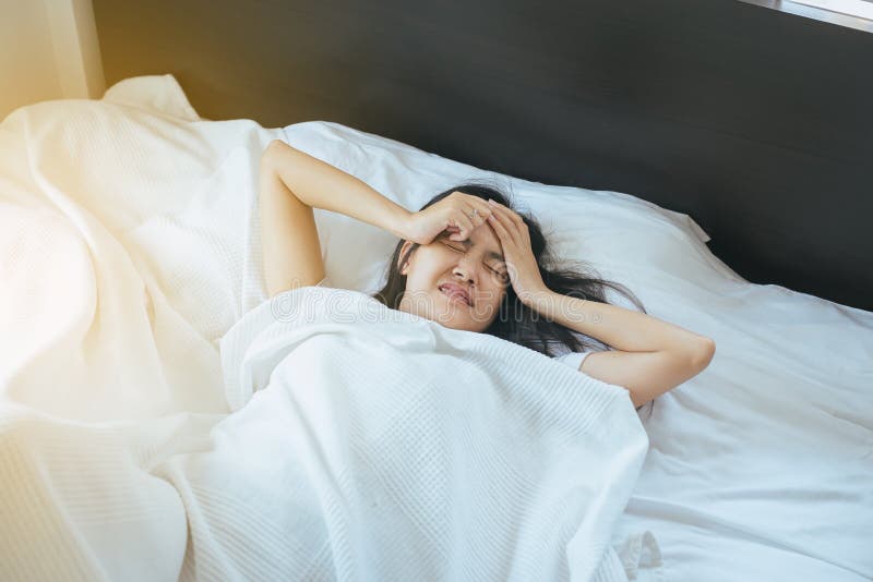 A mulher asiática manda uma dor de cabeça na cama após acordar na manhã foto de stock A mulher asiática manda uma dor de cabeça na cama após acordar na manhã foto de stock