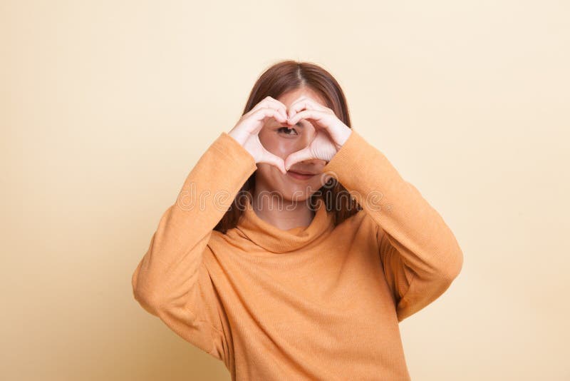 A mulher asiática nova bonita faz o sinal da mão do coração foto de stock A mulher asiática nova bonita faz o sinal da mão do coração foto de stock