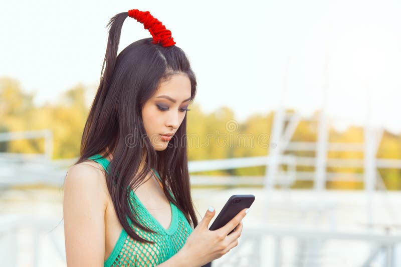 Mulher asiática nova feliz com o smartphone que está na rua imagens de stock royalty free Mulher asiática nova feliz com o smartphone que está na rua imagens de stock royalty free
