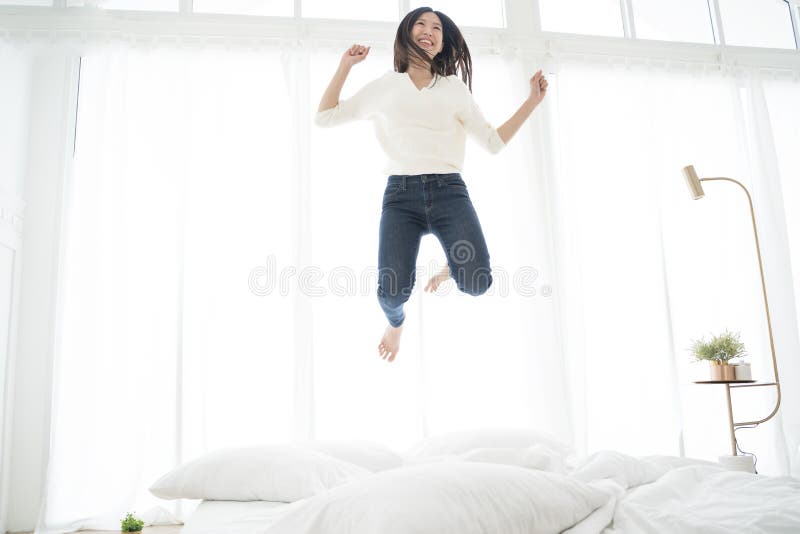 Mulher asiática que salta na cama Conceito feliz foto de stock Mulher asiática que salta na cama Conceito feliz foto de stock